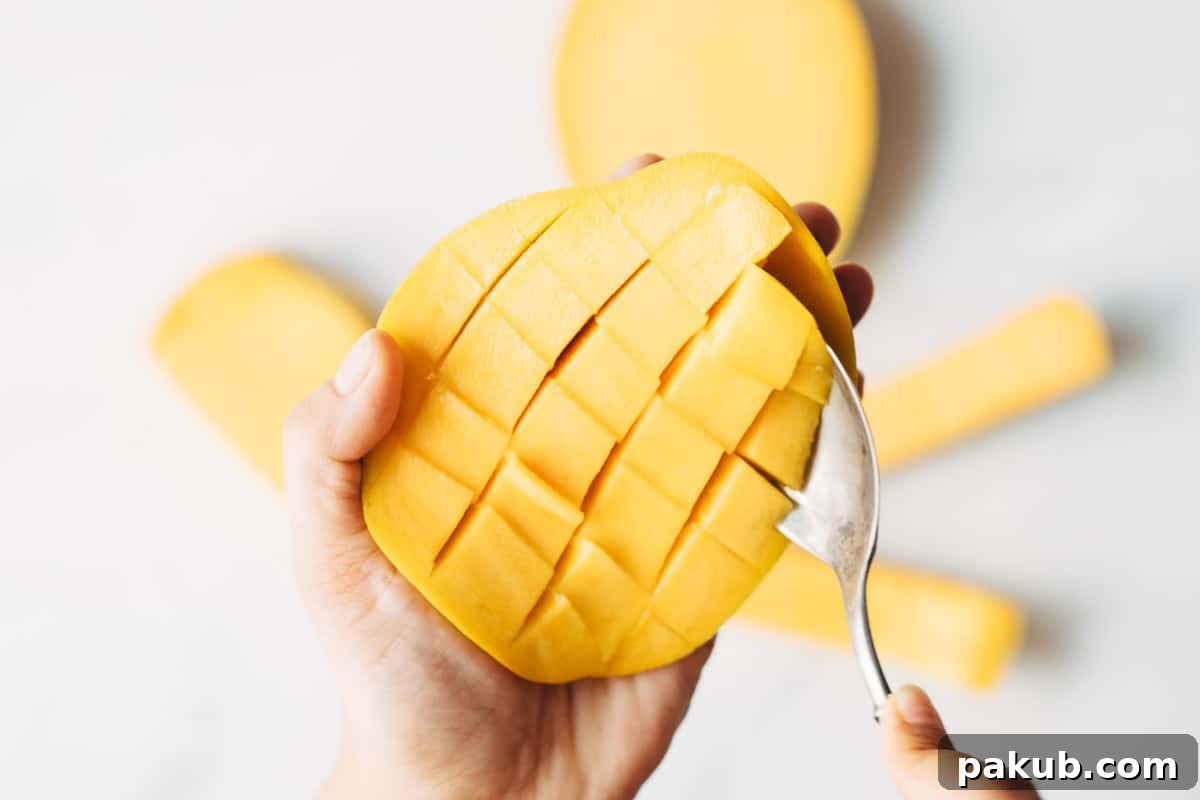 Easy Step-by-Step Guide to Cutting a Mango 9 A spoon efficiently scooping out neat, unpeeled mango dices from a scored mango cheek, showcasing a quick and clean method.