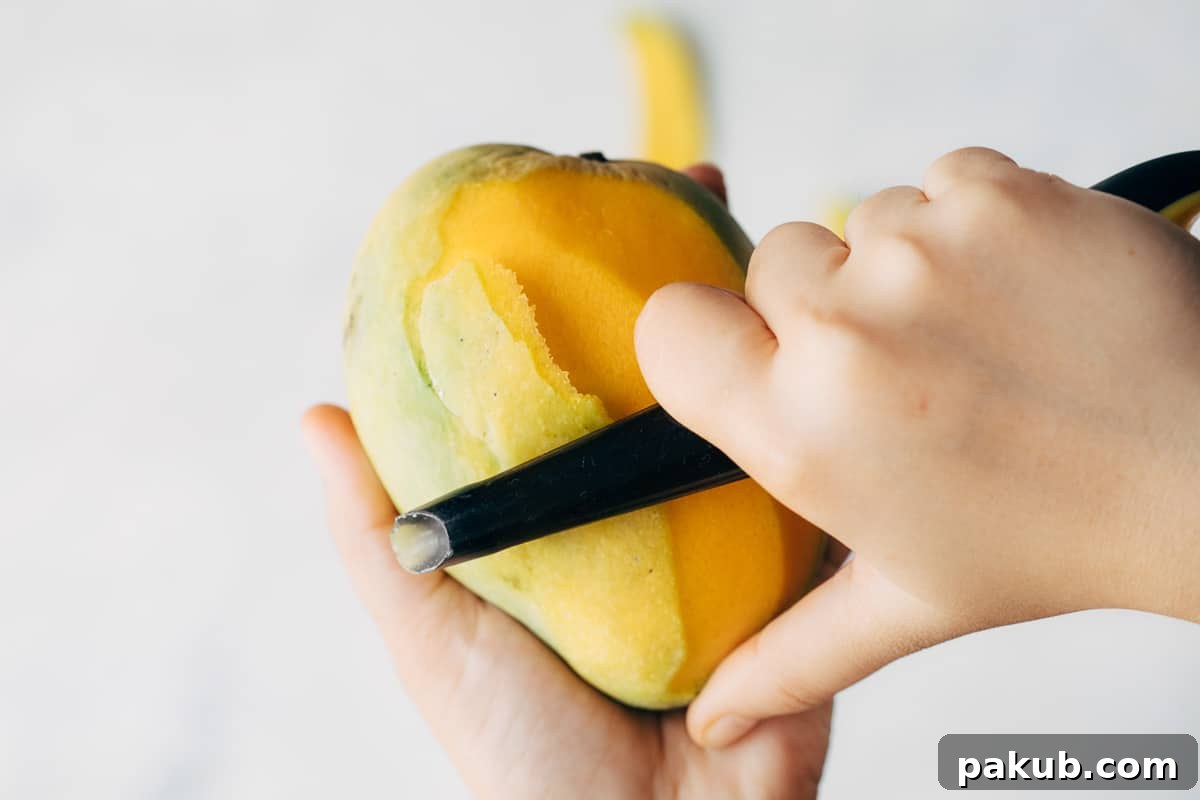 Easy Step-by-Step Guide to Cutting a Mango 10 A ripe mango being skillfully peeled with a black vegetable peeler, ensuring minimal waste of the luscious fruit beneath.