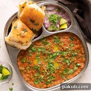 Pav Bhaji served in a steel plate with ladi pav, onions and coriander on the side