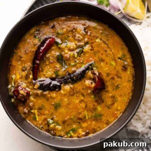A bowl of Dhaba style Moong Dal served with rice and sliced onions on a plate