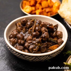 Bowl of pindi chole served with bhatura and potatoes on the side
