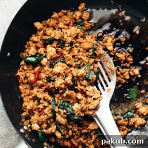 thai basil chicken being in cooked in a wok with a steel spatula