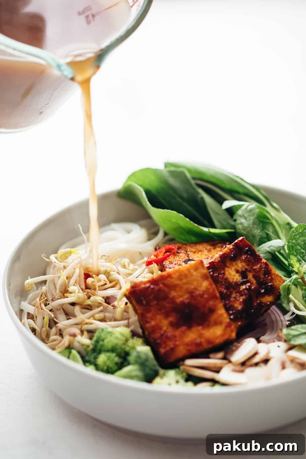Plant-Powered Pho Bowl 3 Rich, aromatic vegetarian pho broth being poured over a bowl of noodles and fresh vegetables.