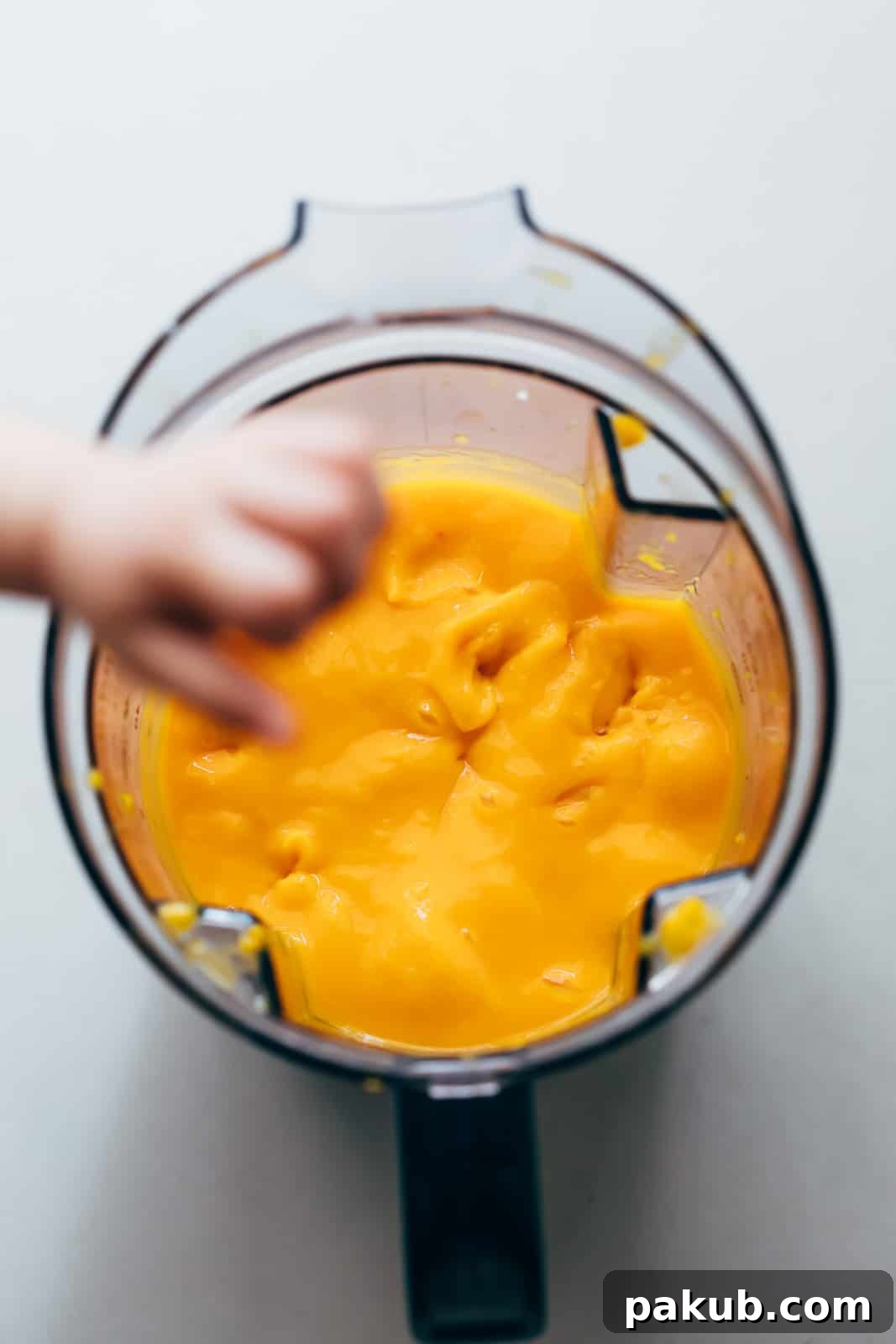 Vibrant mango puree in a blender, ready to be incorporated into the cheesecake mixture