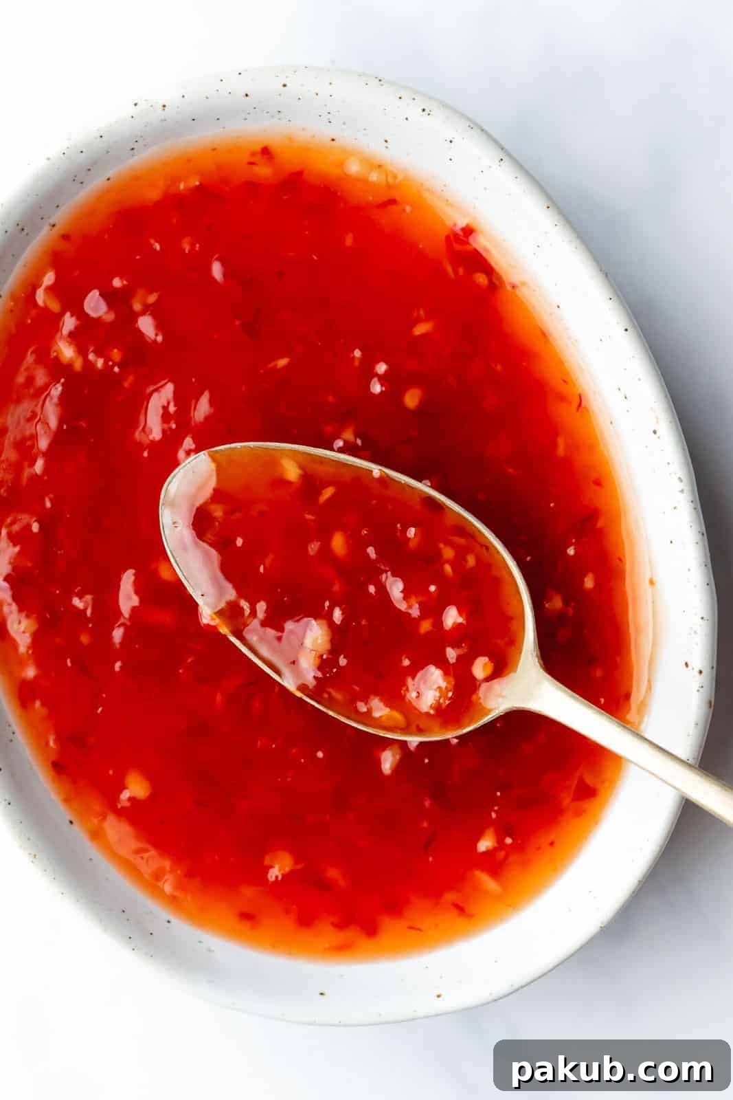 Thai sweet chili sauce served in a bowl with a spoon in it, showcasing its glossy texture