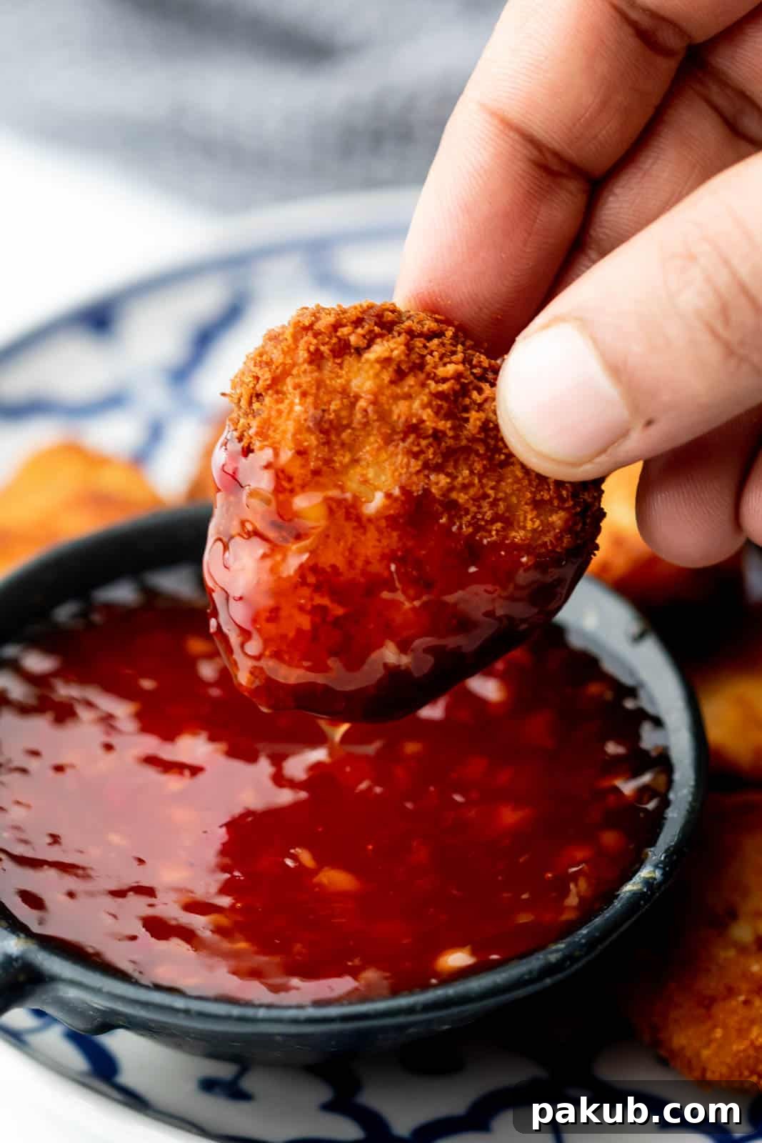 An image of a chicken nugget being dipped into a bowl of glossy homemade Thai sweet chili sauce