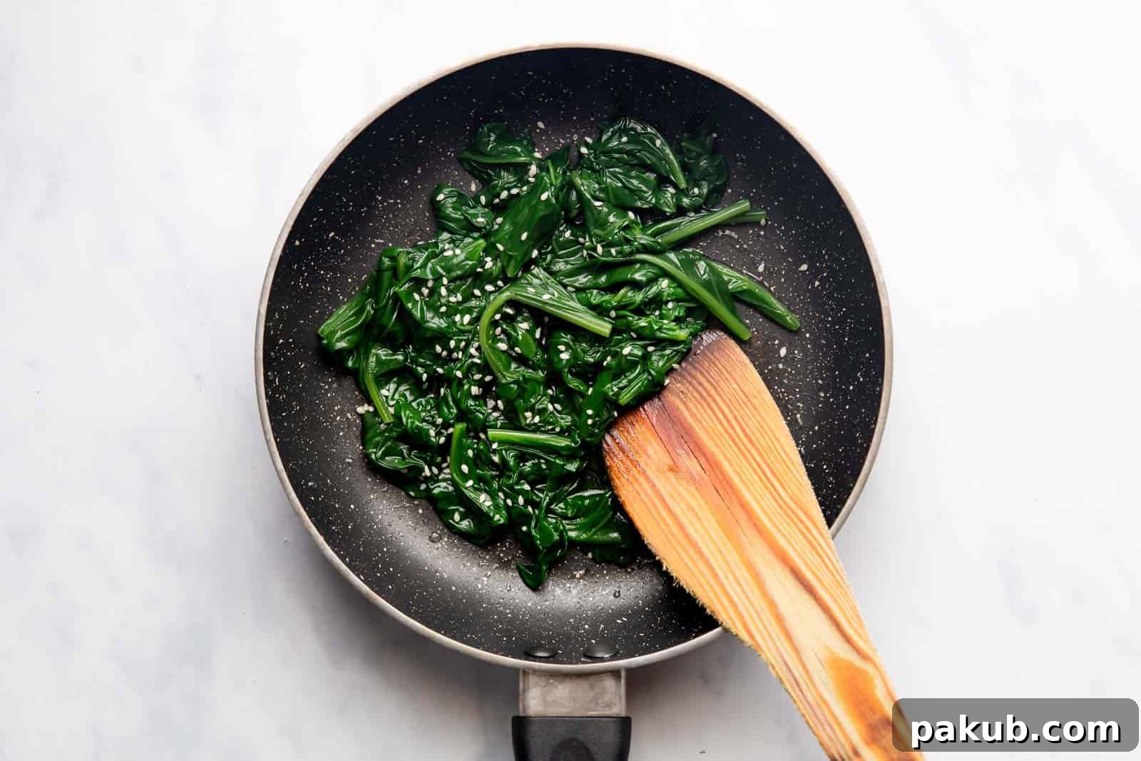 Spinach Magic Three Ways From Pan to Freezer 6 Perfectly sautéed spinach in a pan, garnished with a sprinkle of sesame seeds, ready to serve