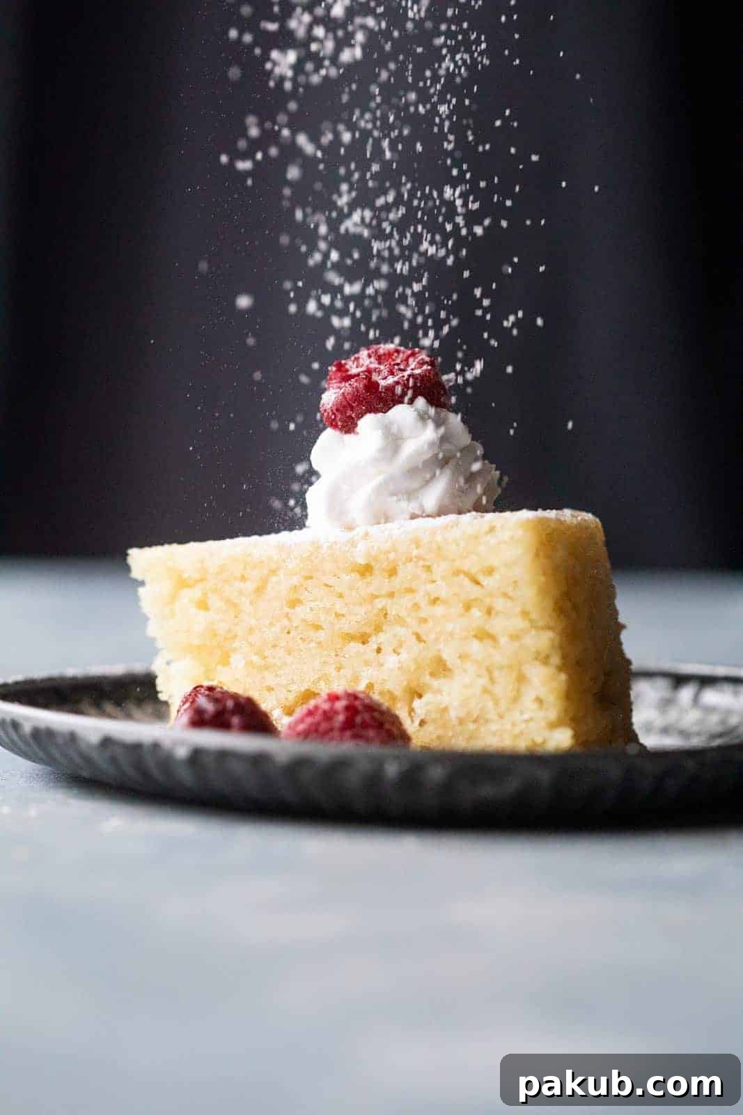 Velvety Soft & Moist Eggless Vanilla Cake 2 A beautifully sliced eggless vanilla cake, perfectly moist, topped with whipped cream, fresh raspberries, and a delicate dusting of icing sugar.