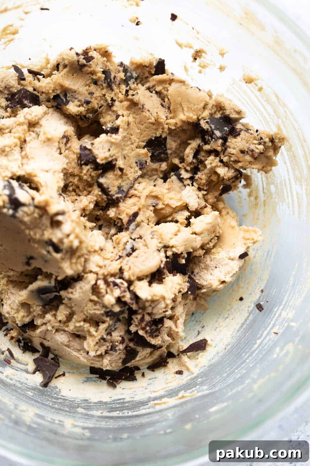 A large glass bowl filled with perfectly mixed and chilled eggless chocolate chip cookie dough, featuring visible chocolate chips, ready to be scooped and baked.