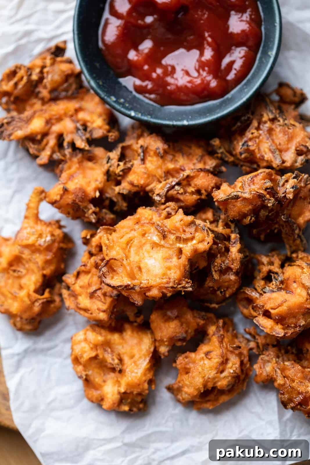 Crispy street-style Onion Pakodas served on a platter with tomato ketchup, perfect for a rainy day snack.