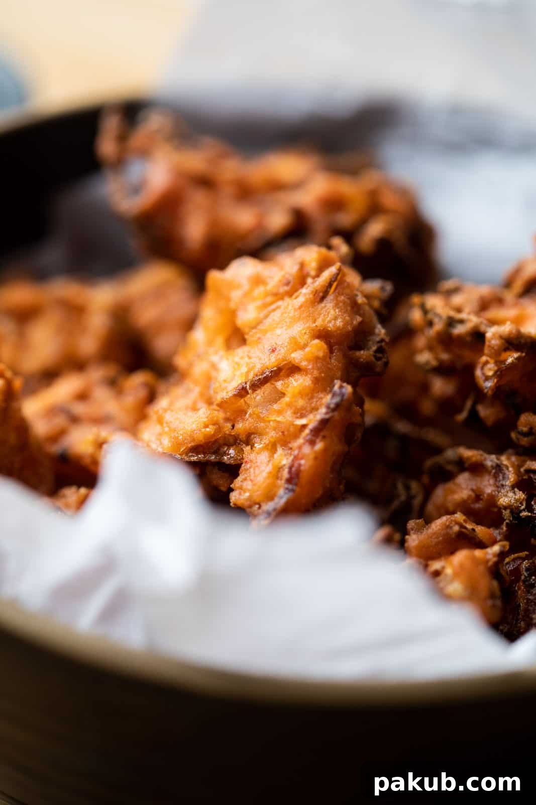 Close-up view of golden-brown, perfectly crispy Onion Pakodas served in a bowl, highlighting their texture.
