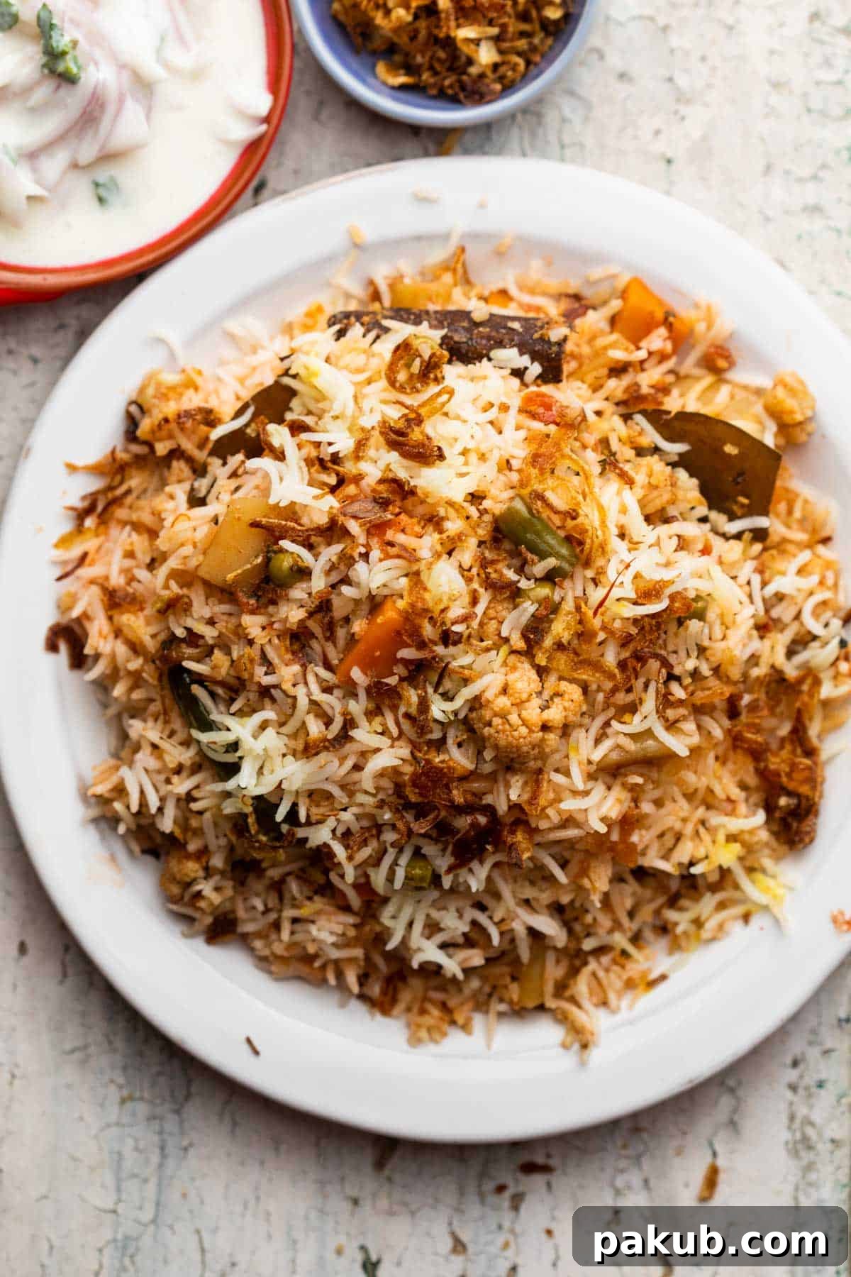 Mastering Delicious Vegetable Biryani 7 A beautifully plated Veg Biryani garnished with crispy fried onions, served alongside a refreshing bowl of raita.