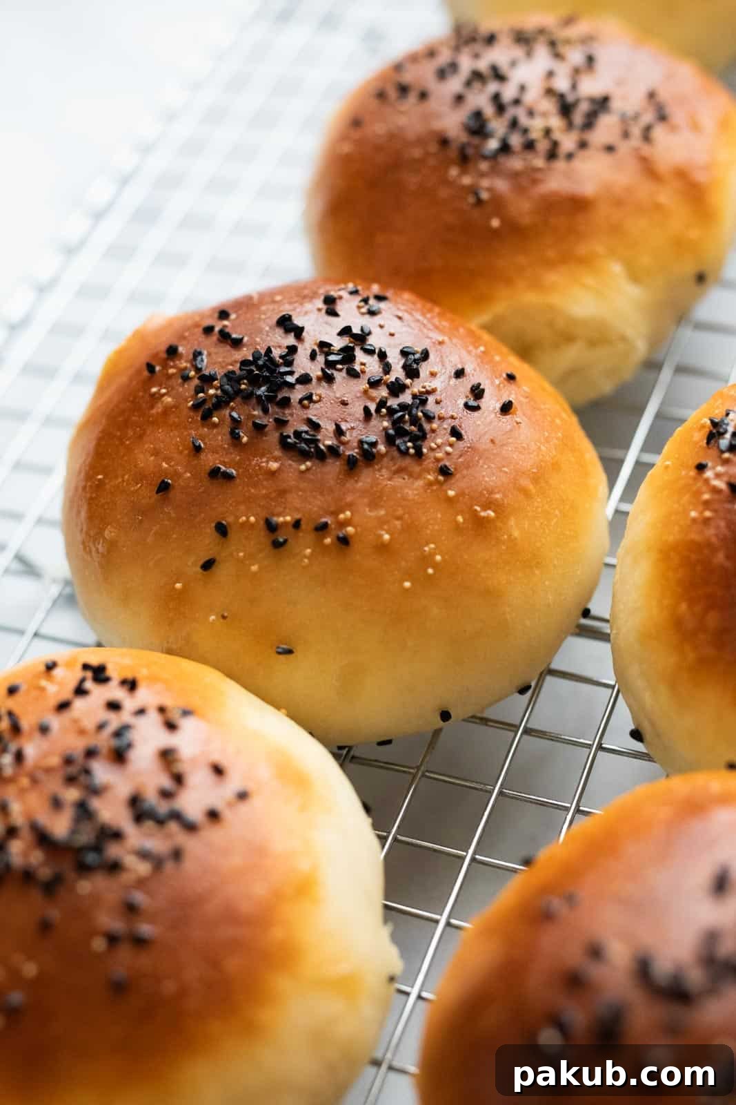Freshly baked bread buns cooling on a wire rack, perfectly golden and risen.