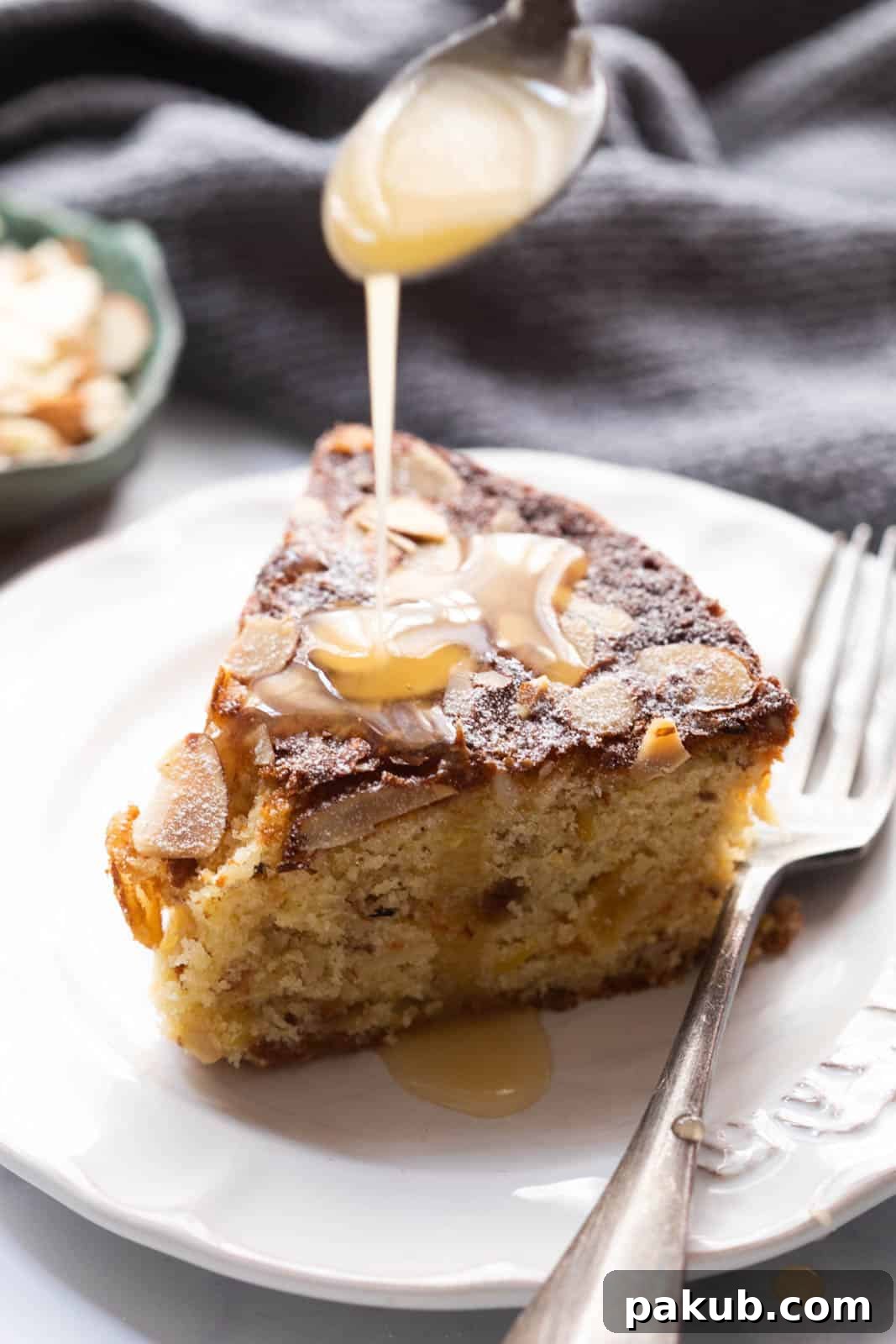 Scottish Dundee Cake: A Festive Delight 2 Pouring bright orange glaze over a delectable slice of Scottish Dundee cake, adorned with almonds, on a pristine white plate.