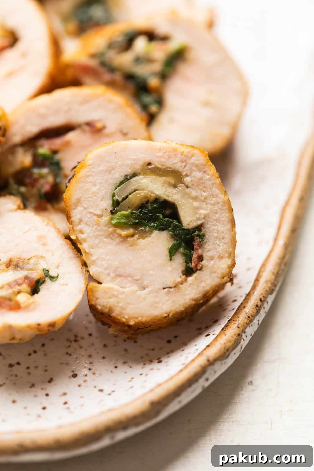 Closeup of a slice of chicken roulade to show the layers and the savory stuffing inside