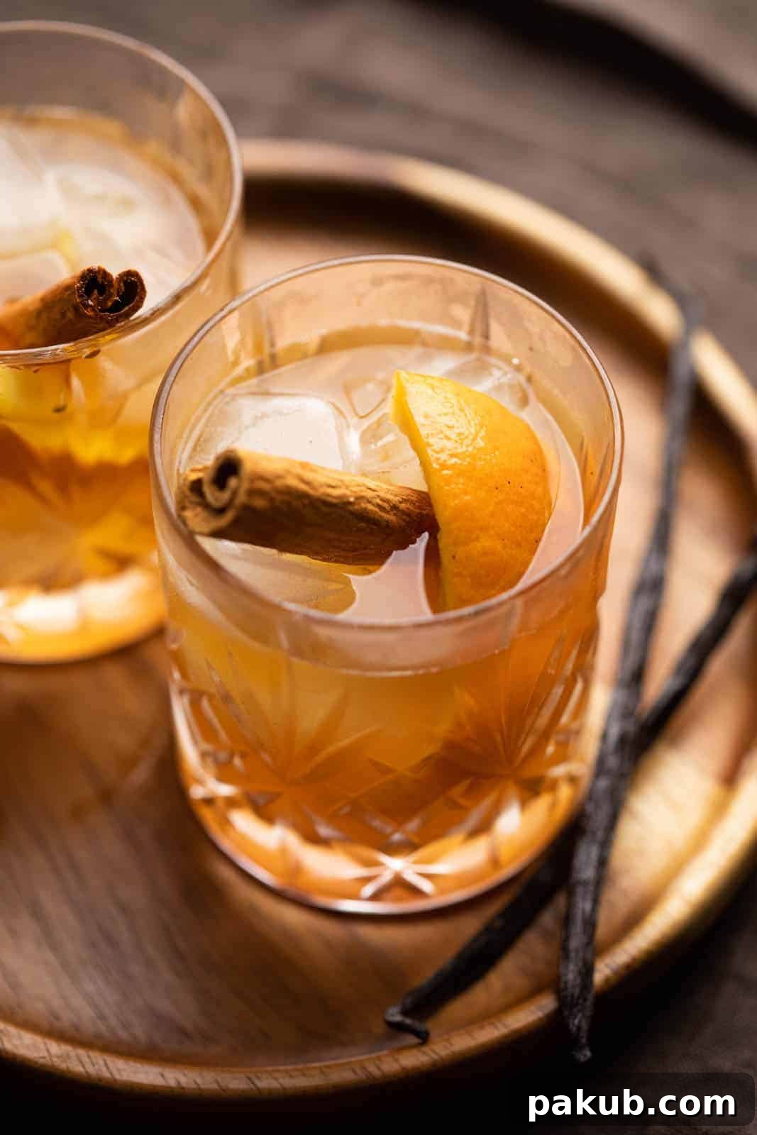 Golden Spiced Old Fashioned 2 A glass of vanilla cinnamon old fashioned on a tray with vanilla beans on the side, evoking warmth and comfort.