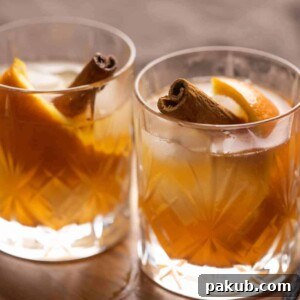 Two glasses of vanilla cinnamon old fashioned served side by side, garnished with orange peel and cinnamon sticks.