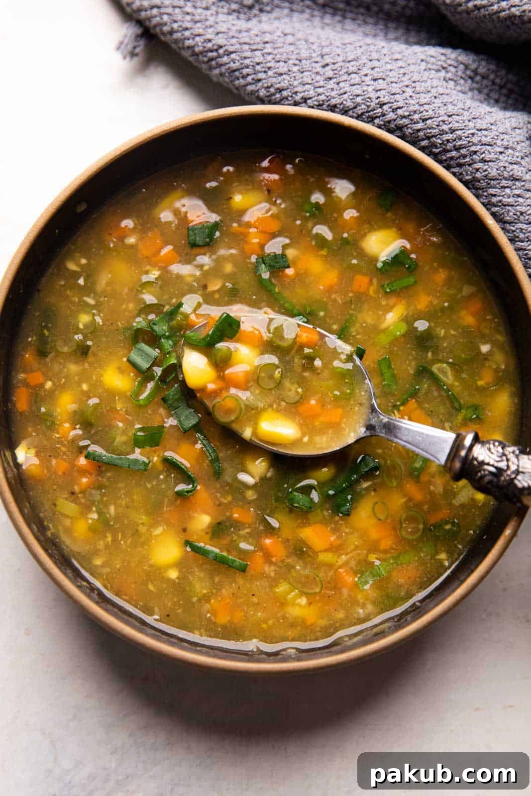 A rich and creamy Vegetarian Sweet Corn Soup served in an elegant black bowl with a spoon, garnished subtly.