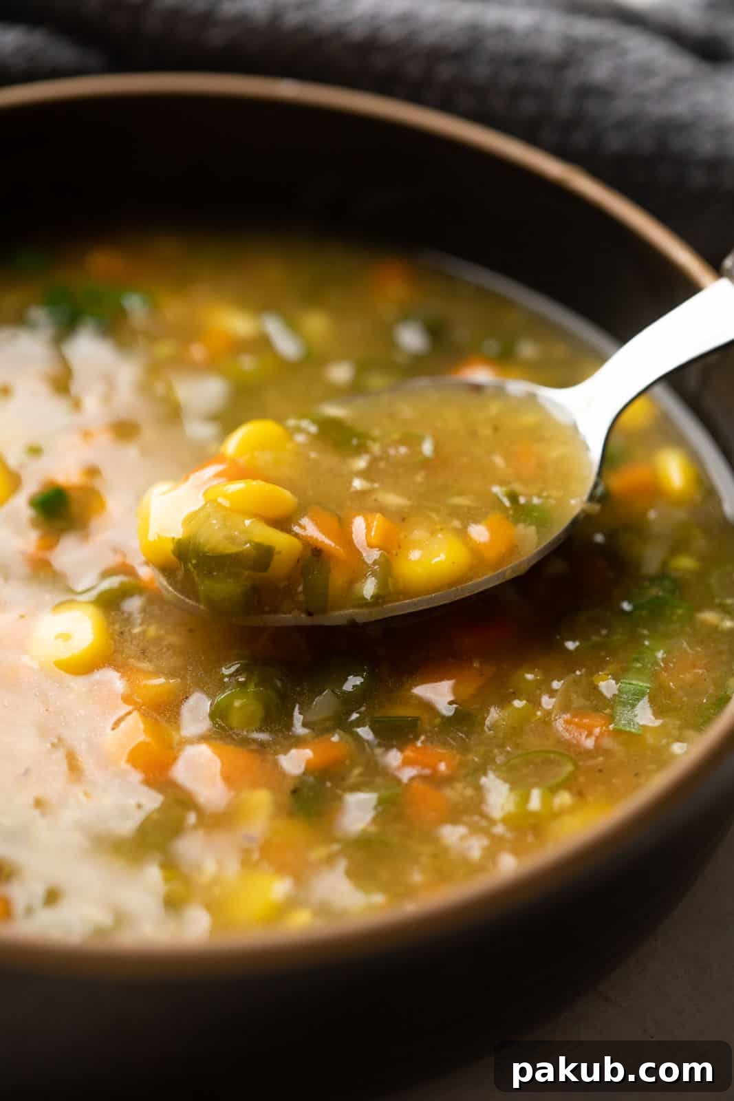 Close-up of a spoonful of creamy vegetarian sweet corn soup, showcasing its rich texture and the finely chopped vegetables and whole corn kernels.
