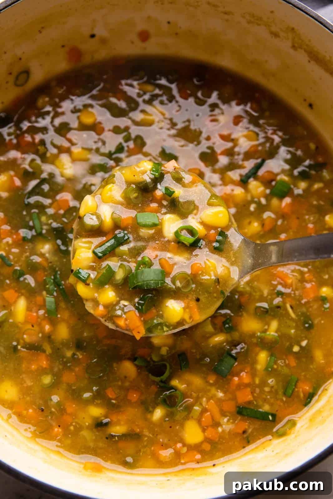 A ladle serving a generous portion of creamy sweet corn soup directly from the cooking pot, ready to be enjoyed.