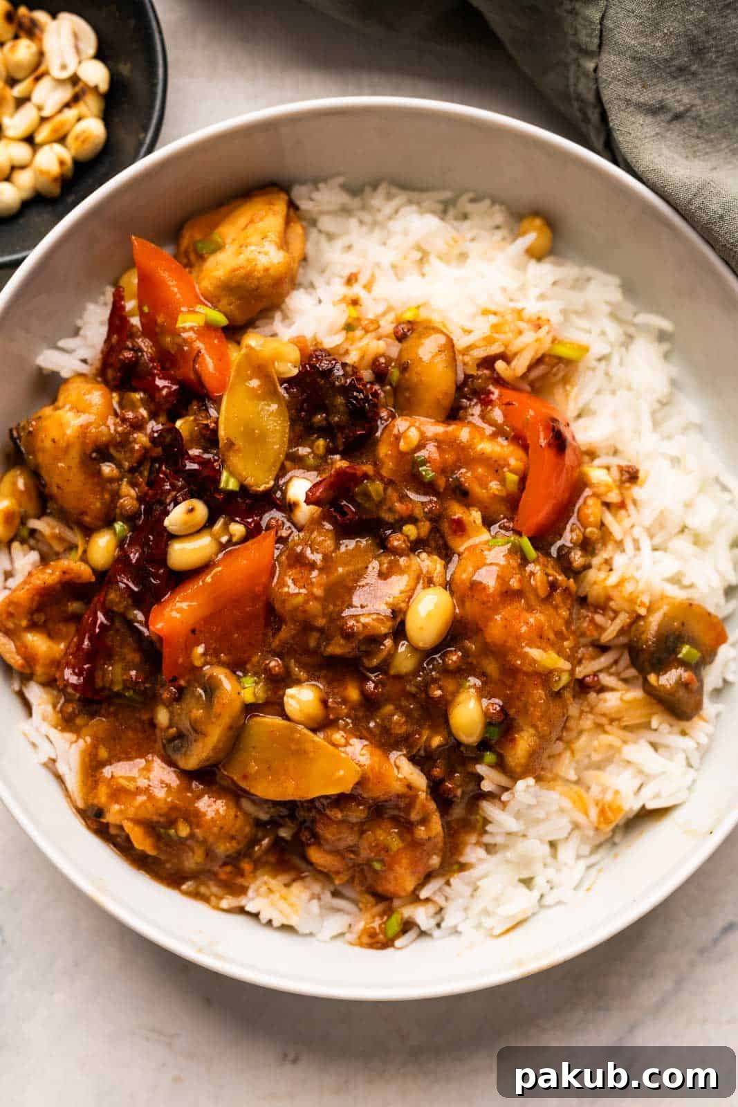 Kung Pao Chicken served attractively over a bed of steamed rice in a bowl, with roasted peanuts scattered on the side.
