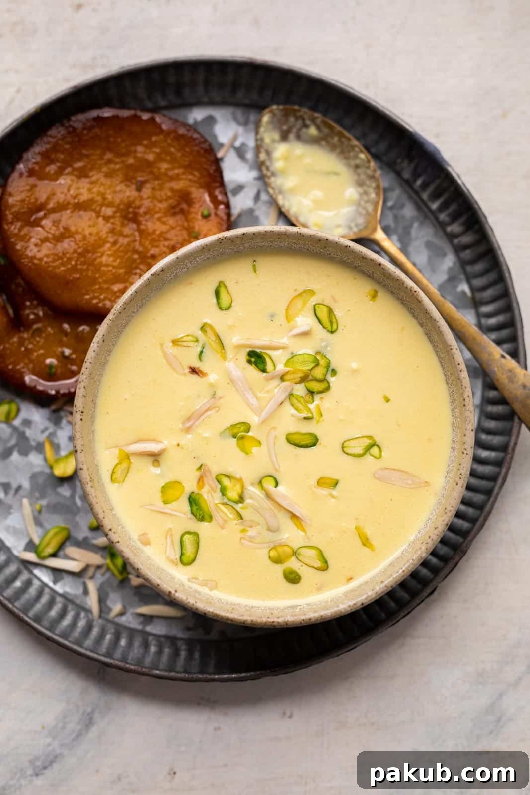 Instant rabdi garnished with slivered almonds and pista served in a brown bowl with malpua on the side.