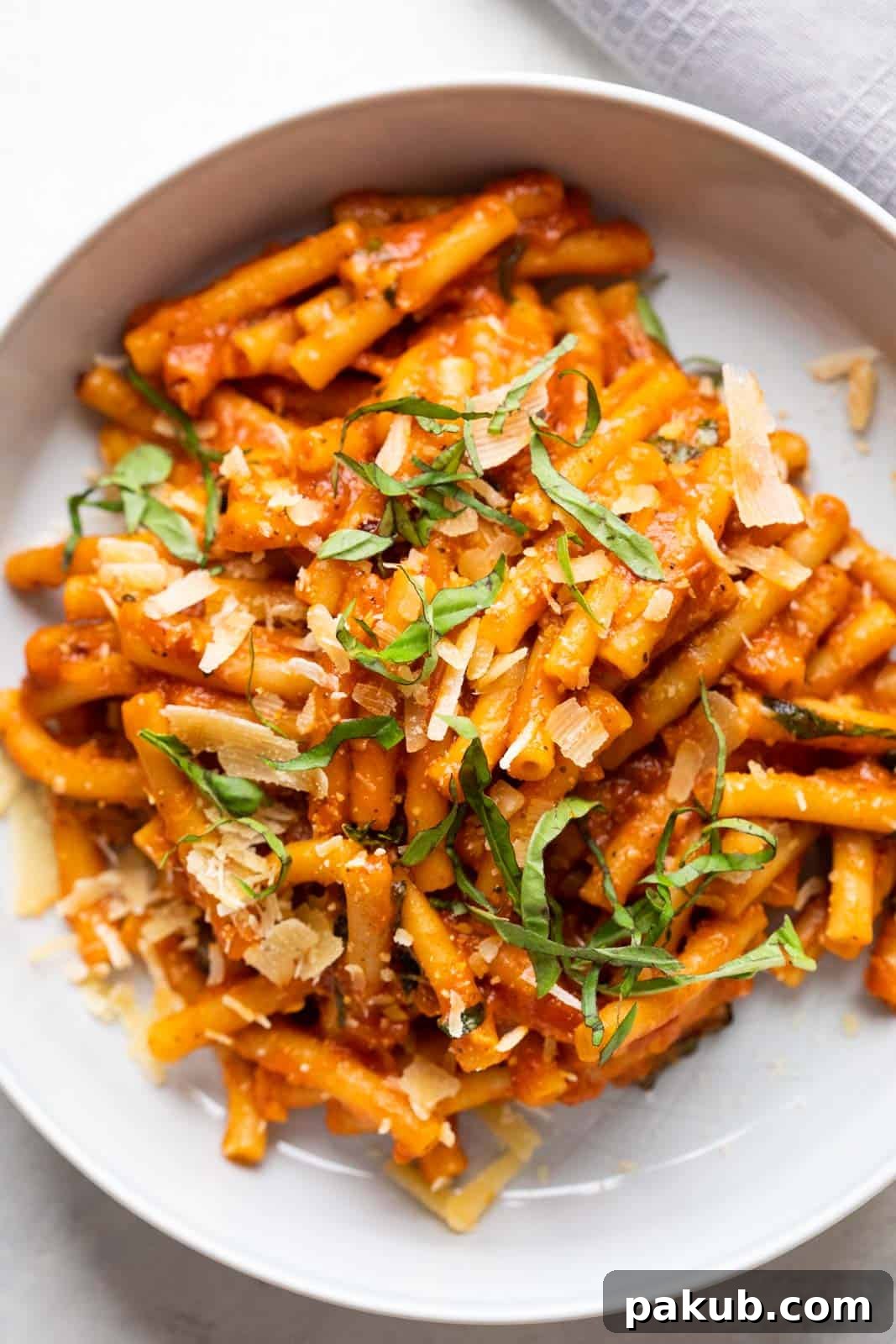 Pasta in red sauce topped with shaved parmesan and basil served in a grey white bowl with a fork on the side
