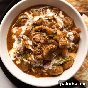 Mushroom masala served in a white bowl with a drizzle of cream on top with paratha on the side