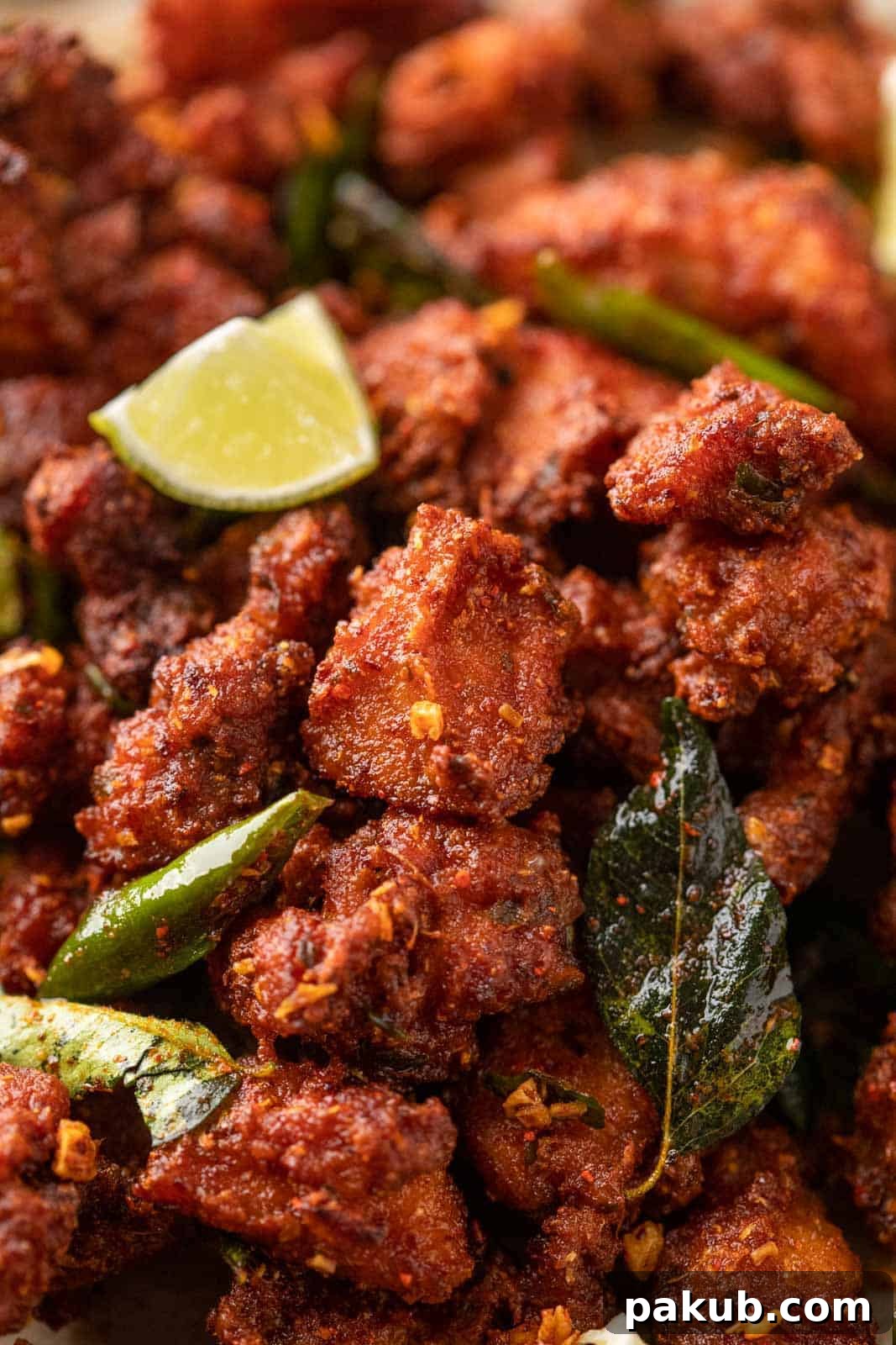 Fiery Crunch Chicken 65 2 Close-up of perfectly crispy, golden-red Chicken 65 nuggets, garnished with fresh curry leaves and halved green chilies, showcasing their mouth-watering texture.