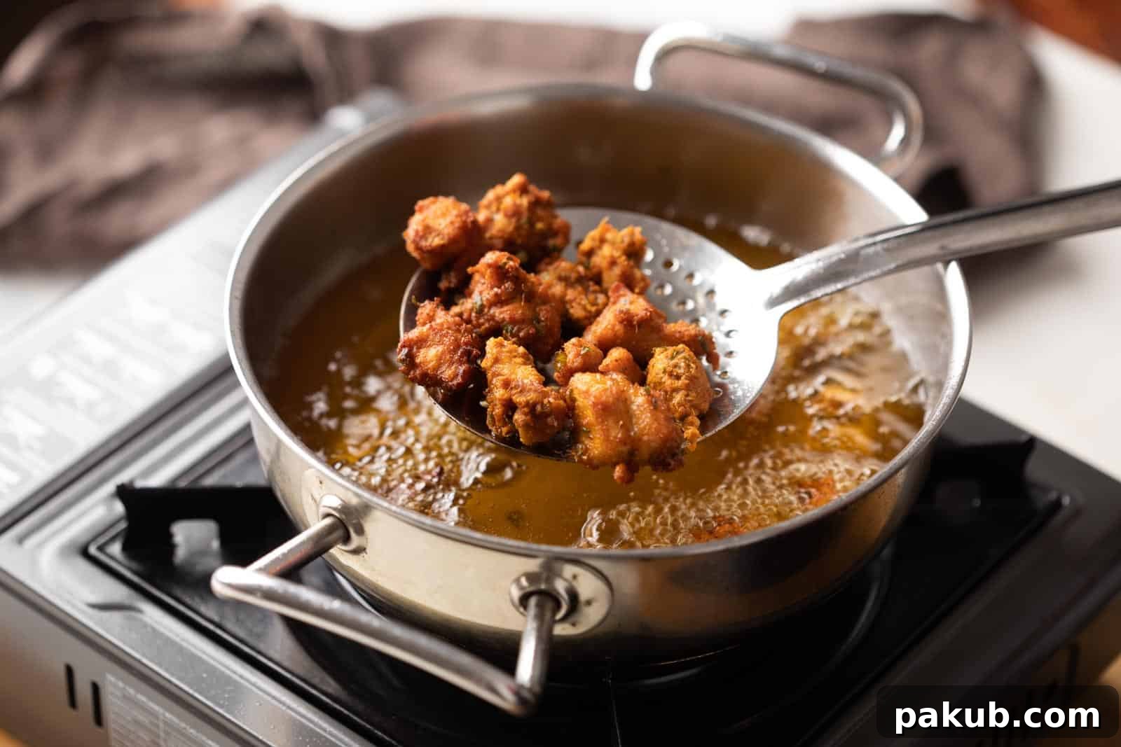 Fiery Crunch Chicken 65 3 Crispy Chicken 65 nuggets being carefully removed from shimmering hot oil in a traditional Indian kadhai, highlighting their vibrant red-golden hue.