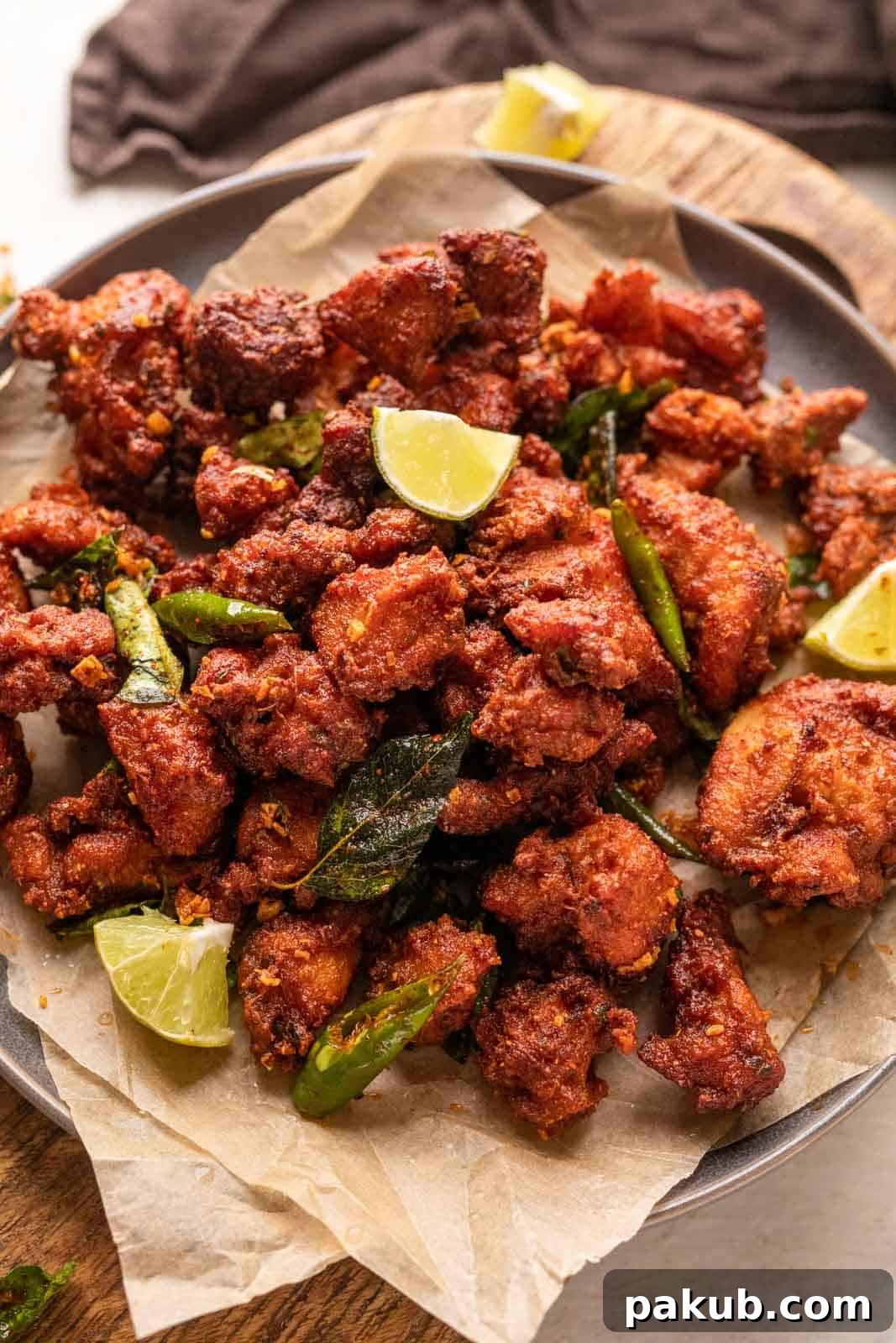 Fiery Crunch Chicken 65 5 Plated Chicken 65, generously garnished with fresh curry leaves, vibrant halved green chilies, and bright lemon wedges, presented beautifully for serving.