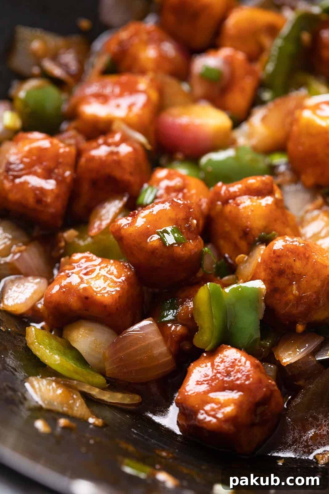 Close up of street style chilli paneer in a wok, garnished with spring onions