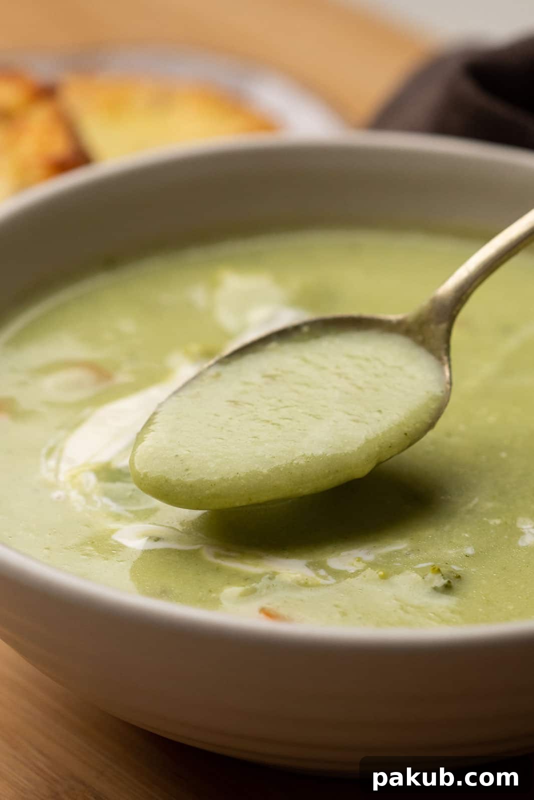 A close-up shot of a spoon scooping a portion of healthy, creamy broccoli soup from a white bowl, showing its thick texture.
