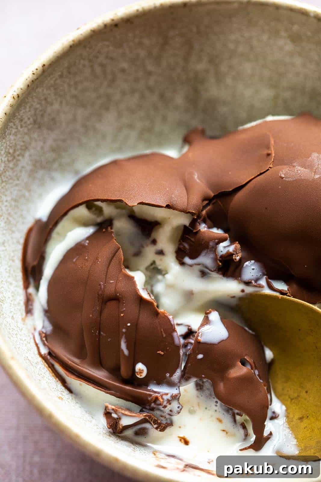 Effortless Two Ingredient Chocolate Magic Shell 5 Close-up of a cracked chocolate magic shell over creamy vanilla ice cream, revealing the inviting texture and showing a spoon ready to dig in, all presented in a rustic brown bowl