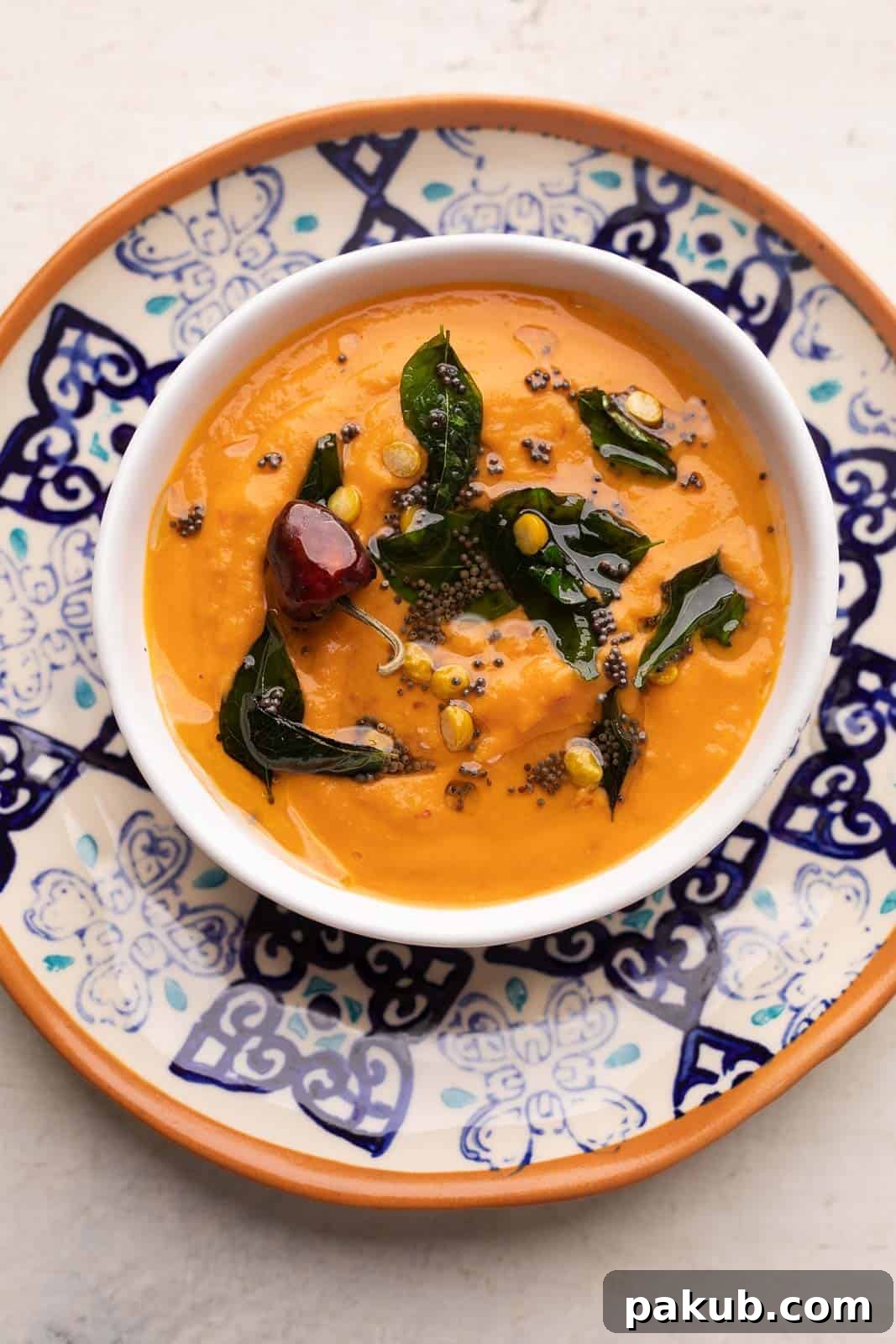 Two Takes on Tomato Chutney 3 South Indian style tomato chutney or thakkali chutney served in a white bowl on a blue and orange plate with tempering on top