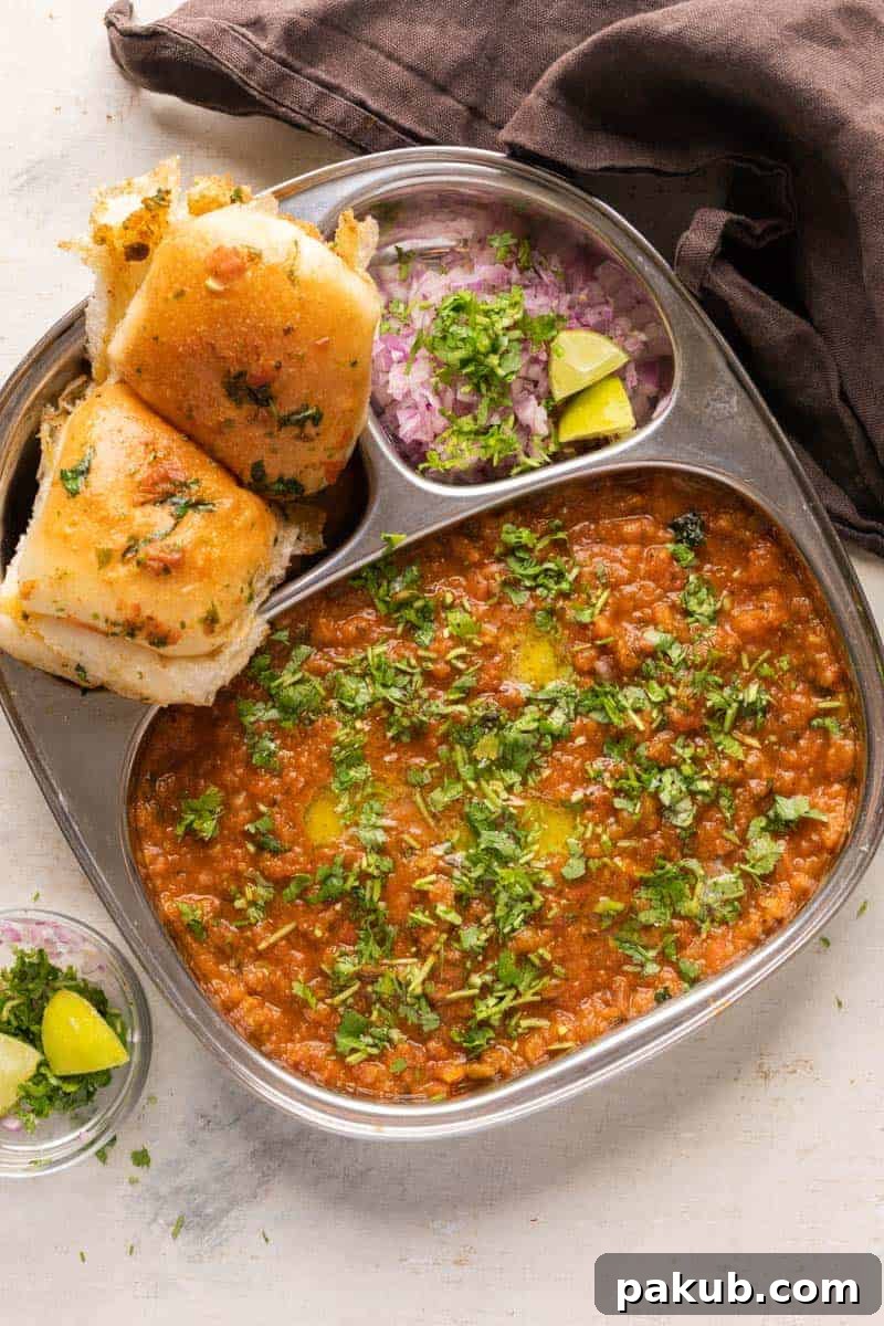 Mumbai Style Pav Bhaji Recipe 2 Pav Bhaji served in a steel plate with ladi pav, onions and coriander on the side