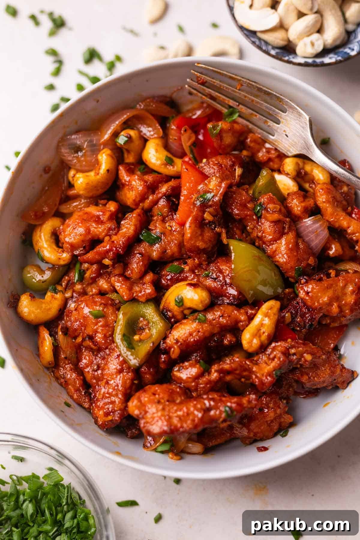 Dragon chicken served in a white bowl with a fork, garnished with spring onions and sesame seeds