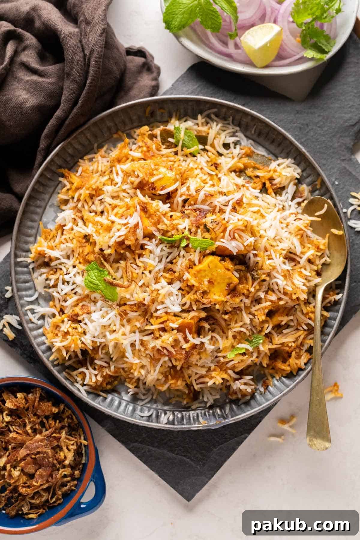Decadent Makhani Paneer Biryani 2 Rich and aromatic Paneer Biryani with Makhani gravy, garnished with fried onions and fresh herbs, served on a grey plate.