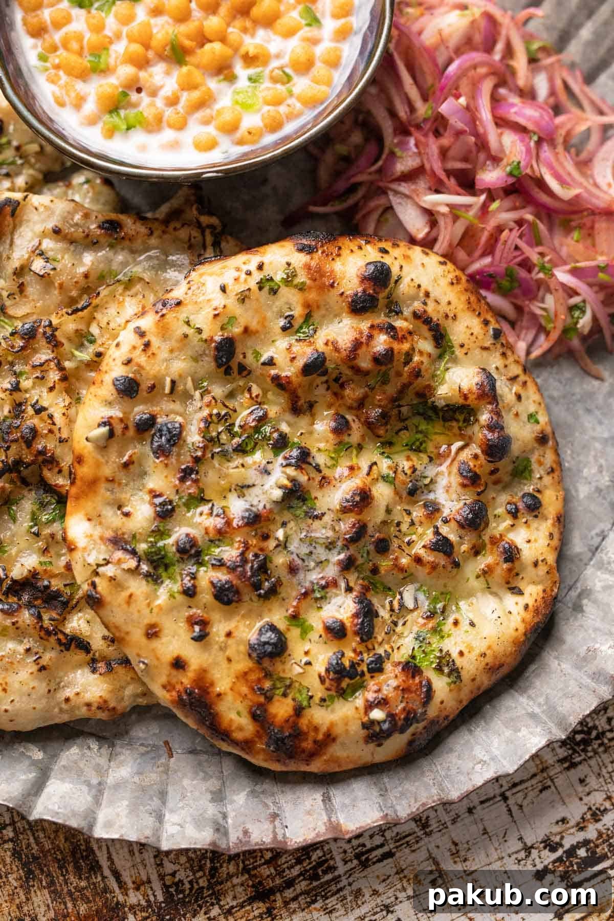 Garlic cheese kulcha served on a plate with pickled onions and boondi raita on the side