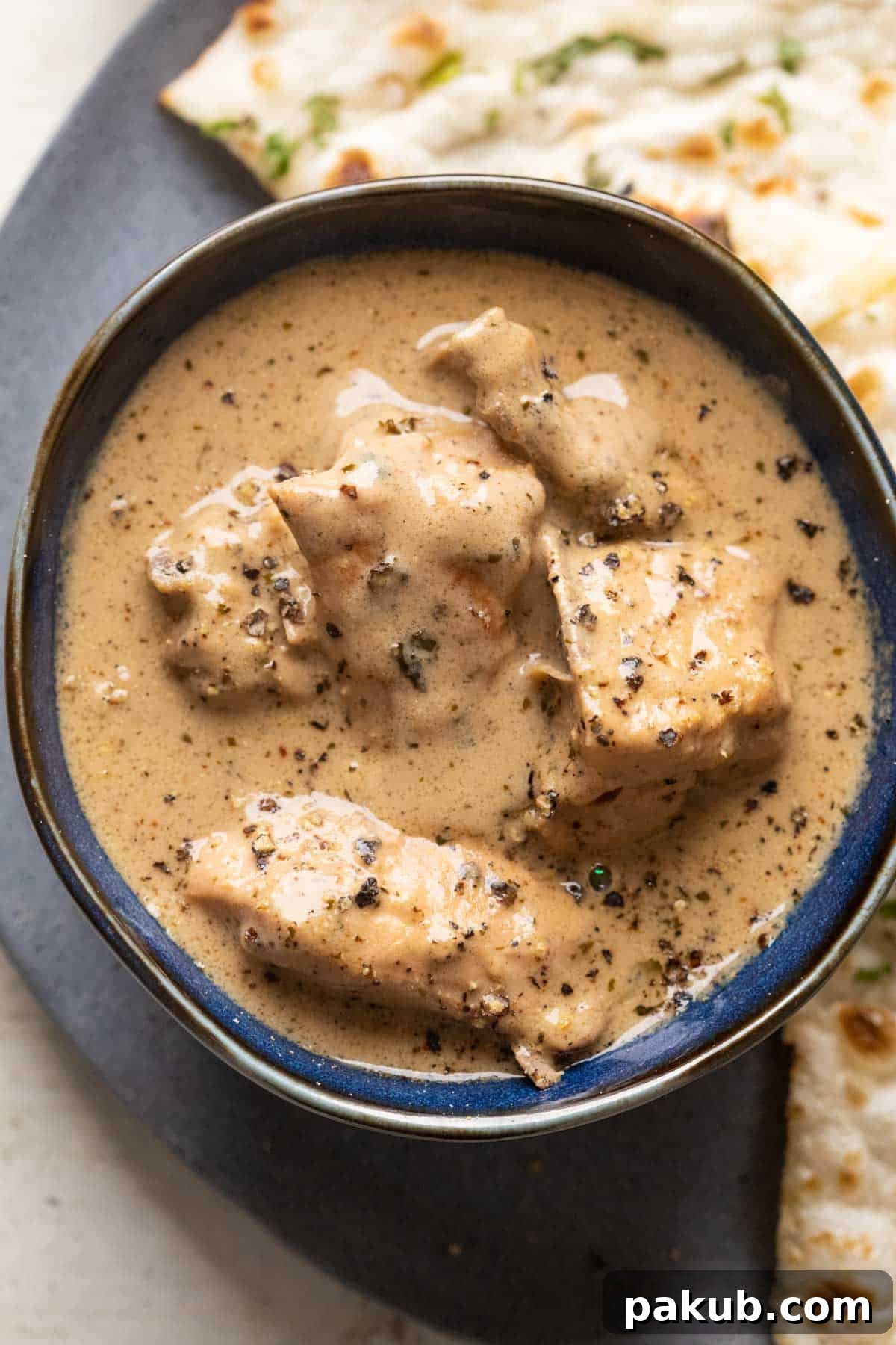 Chicken kali mirch gravy served in a blue bowl with naan on the side, garnished with fresh cilantro
