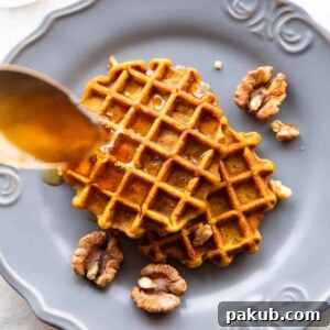 Spoon drizzling honey over two pumpkin waffles served on a plate
