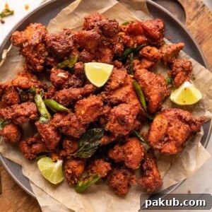 Chicken 65 served on a plate with lime wedges, fried curry leaves and green chillies
