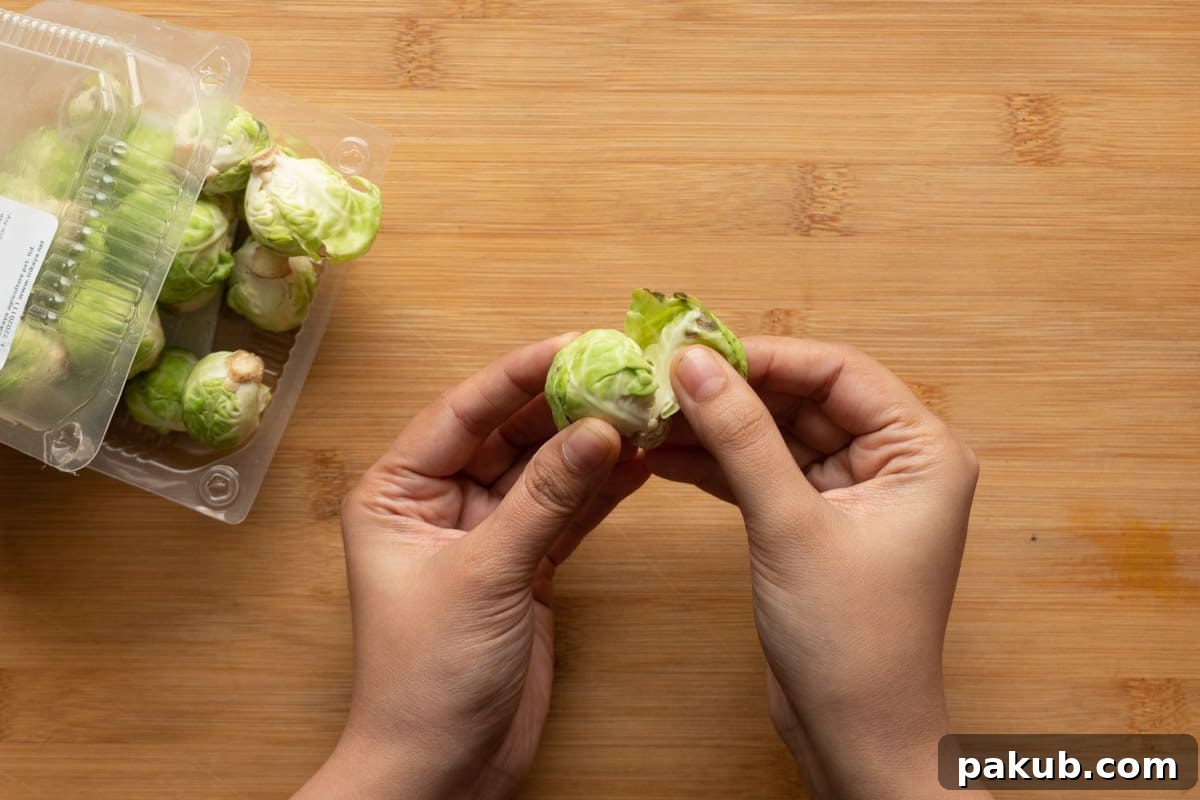 Close-up image depicting fresh Brussels sprouts undergoing initial preparation, with outer leaves being meticulously removed and the woody ends neatly trimmed, ready for the next step in the cooking process.