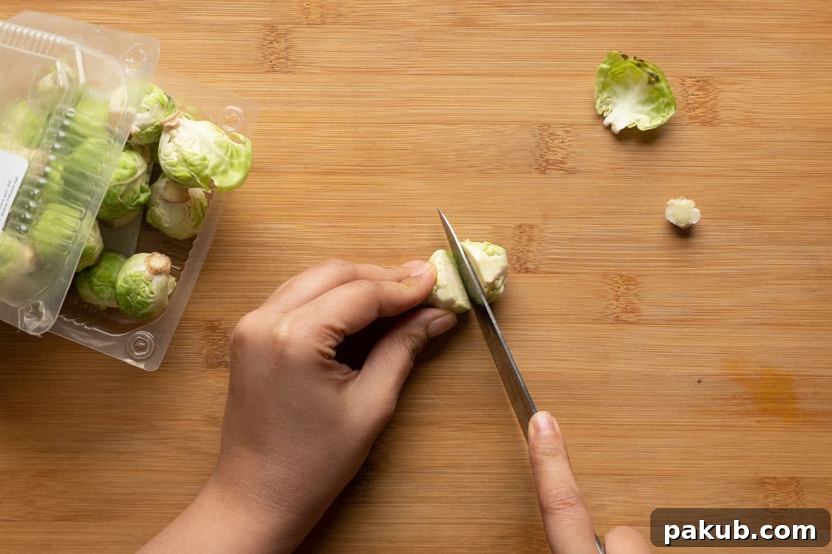 Detailed image illustrating the precise technique of cutting prepared Brussels sprouts in half lengthwise after they have been thoroughly trimmed, showcasing the internal structure ready for seasoning and cooking.