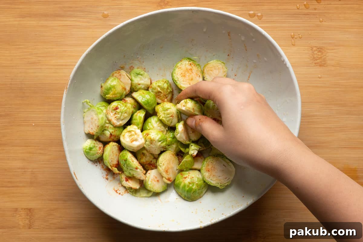 A large mixing bowl containing perfectly coated Brussels sprouts, glistening with olive oil, sweet honey, fragrant garlic powder, and vibrant paprika, thoroughly tossed and ready to be air-fried.
