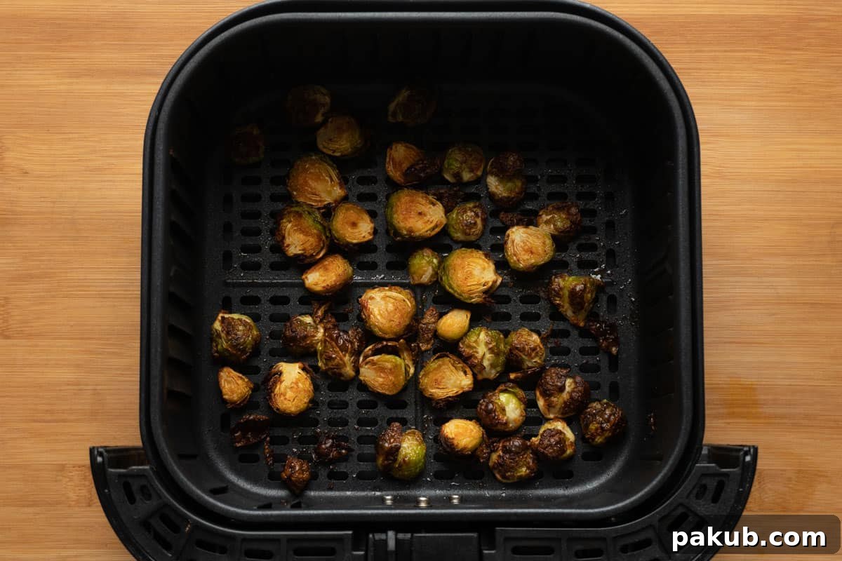A close-up view of perfectly roasted and golden-brown Brussels sprouts, freshly cooked in an air fryer basket, showcasing their irresistible crispy edges and tender appearance.