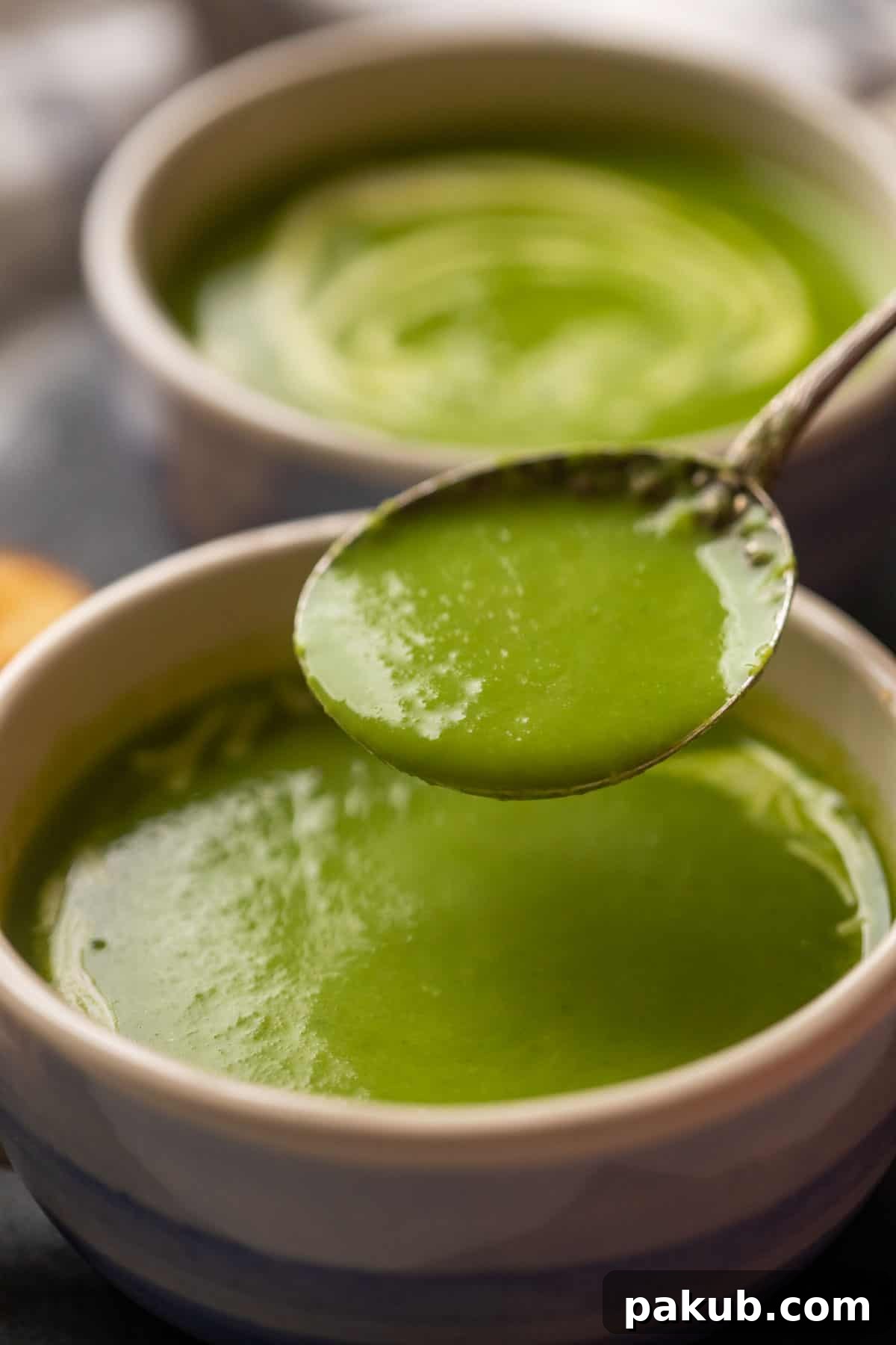 Velvety Spinach Delight 6 A close-up shot of a spoon scooping a generous portion of creamy green spinach soup from a pristine white bowl, highlighting its smooth, rich texture and inviting warmth.