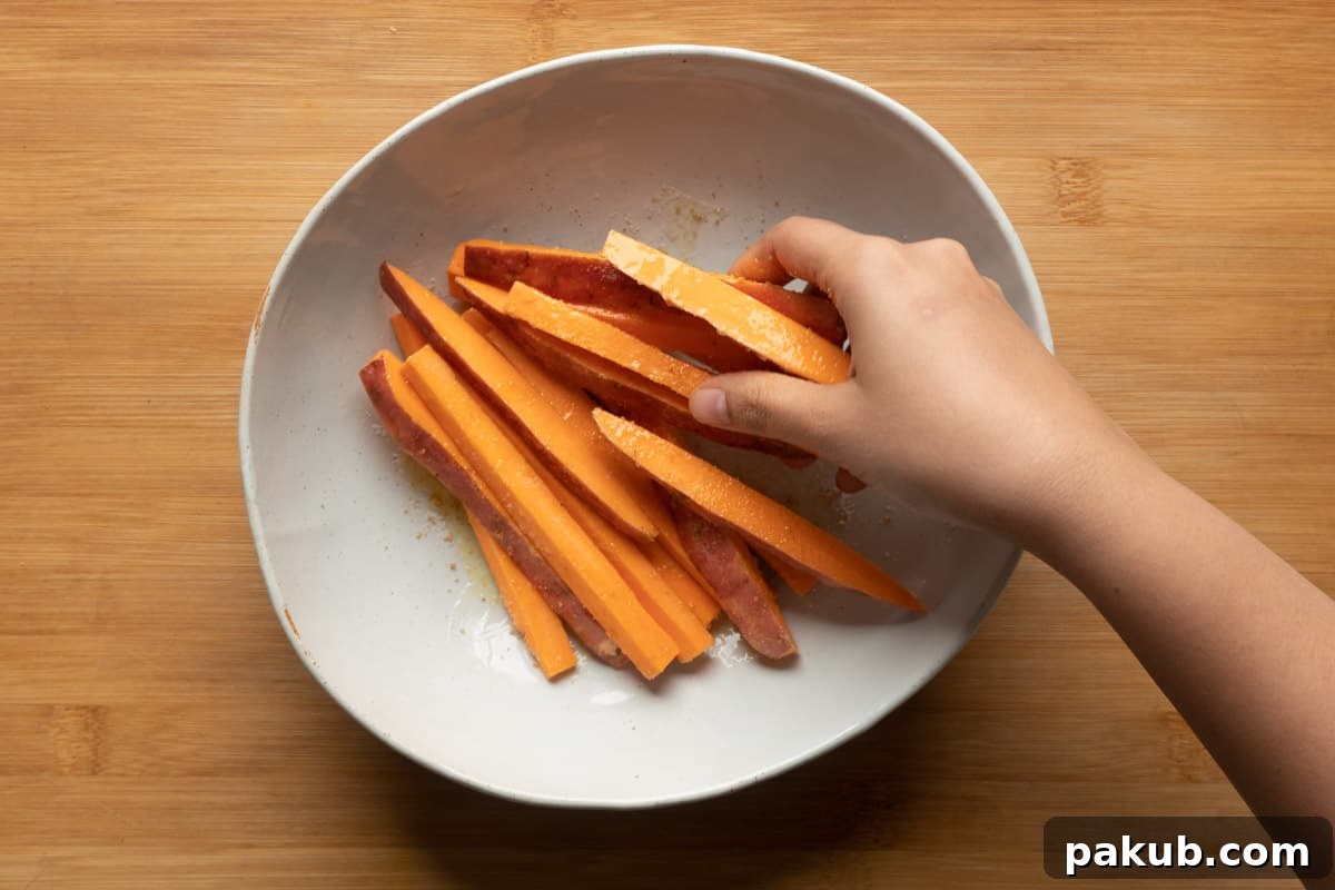 Tossing sweet potato fries with olive oil, salt, and garlic powder in a mixing bowl