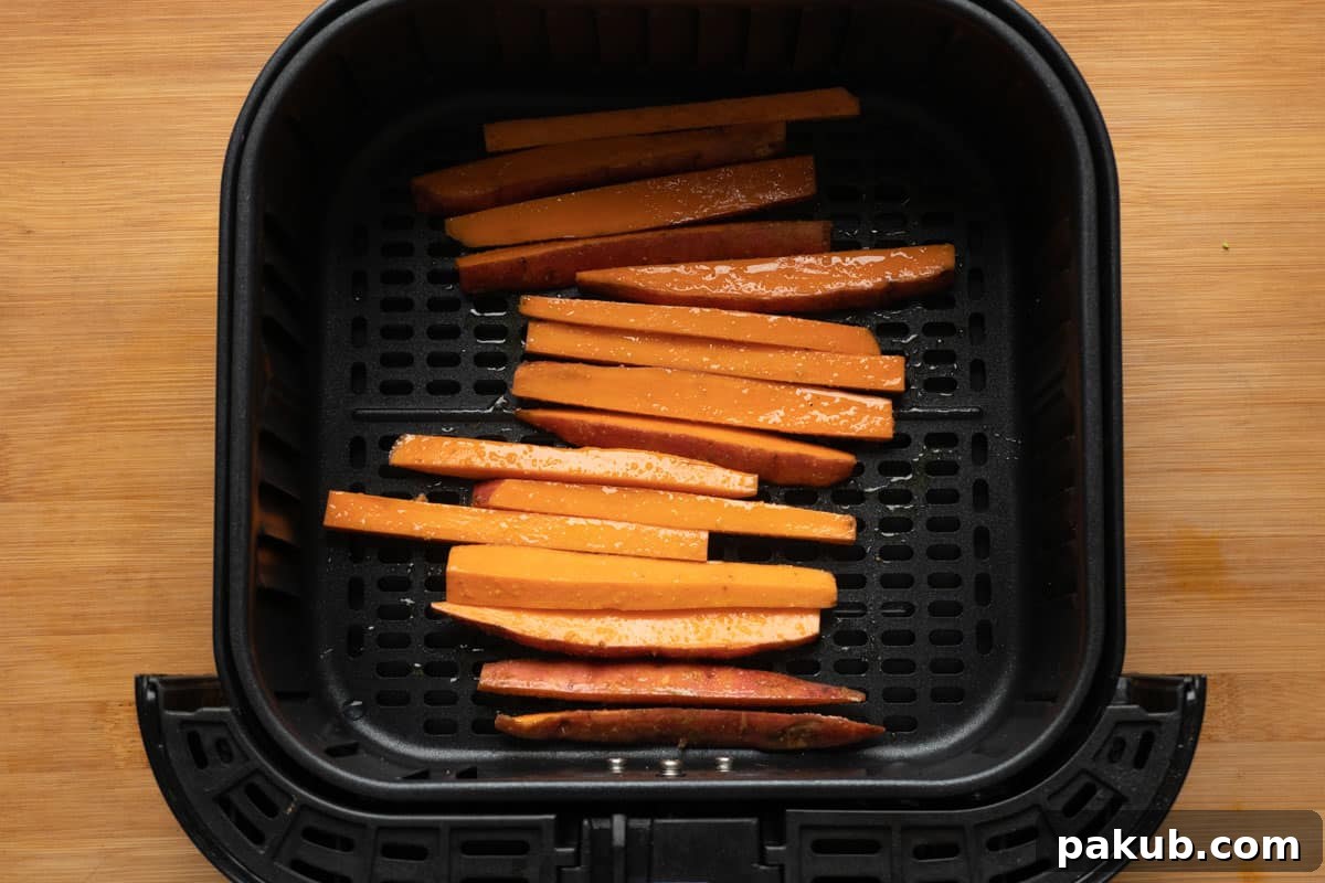 Sweet potato fries carefully arranged in a single layer within the air fryer basket, ready to cook