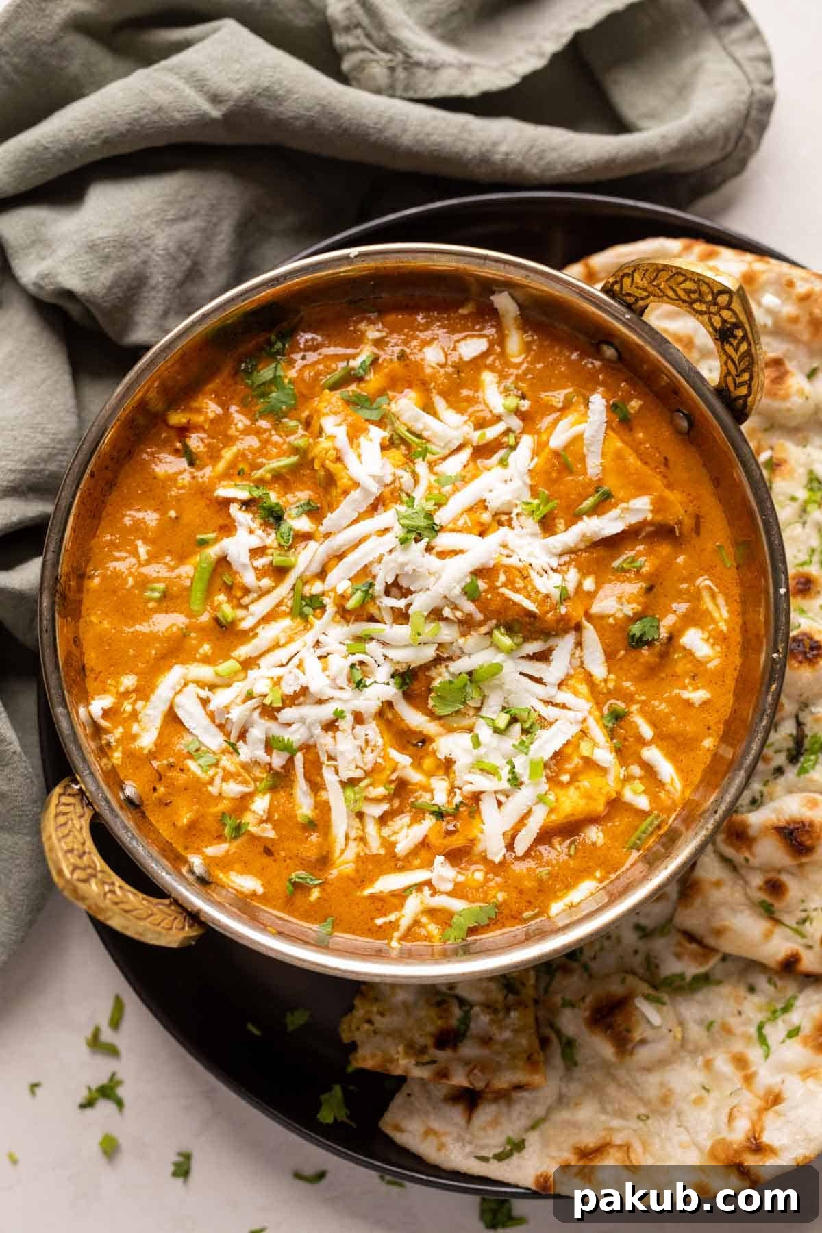 A traditional copper kadhai filled with luscious Paneer Lababdar, garnished with fresh cilantro, served alongside warm naan bread, ready to be enjoyed.